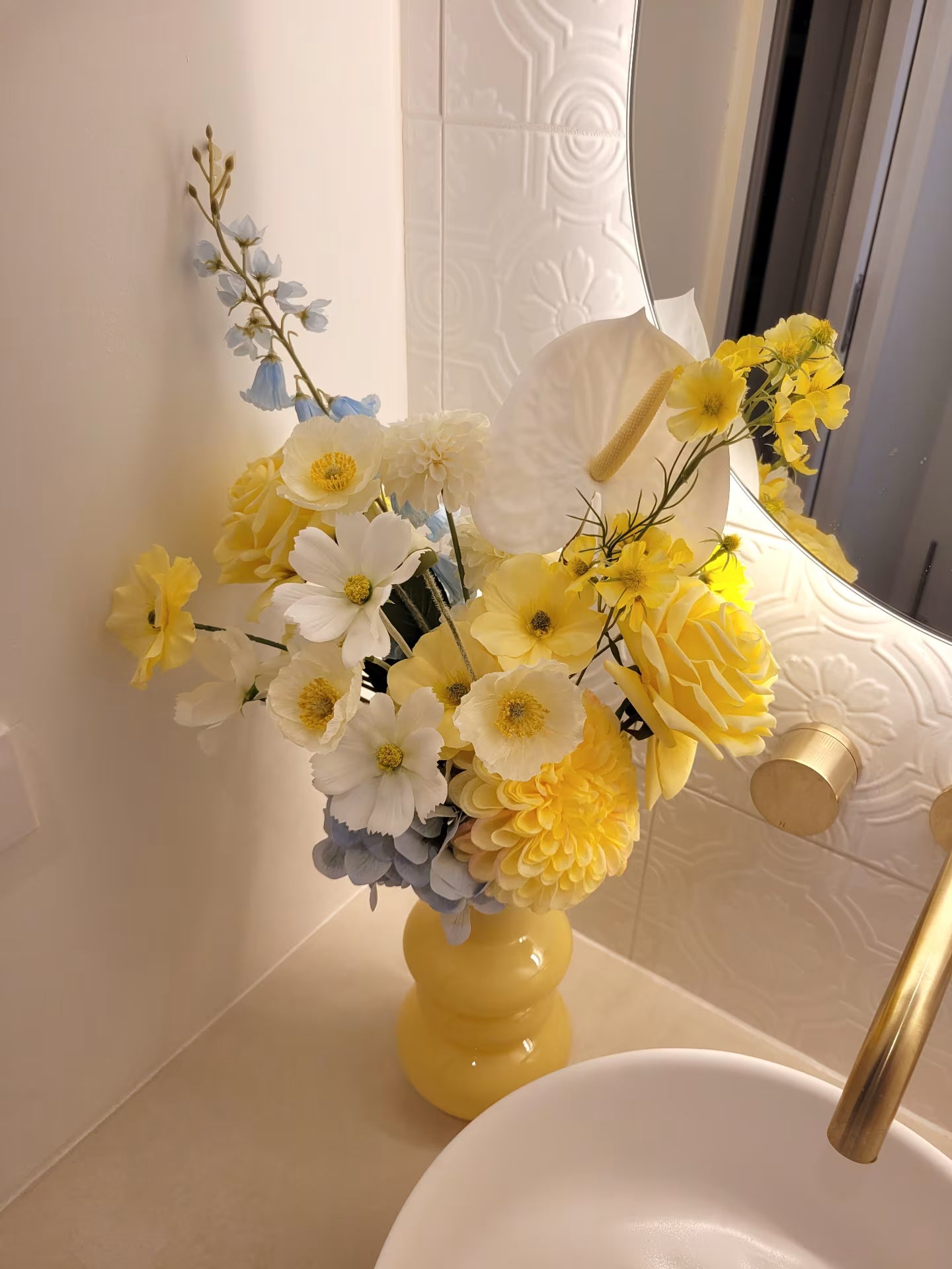 Yellow and white flowers in a yellow vase on a bathroom counter.