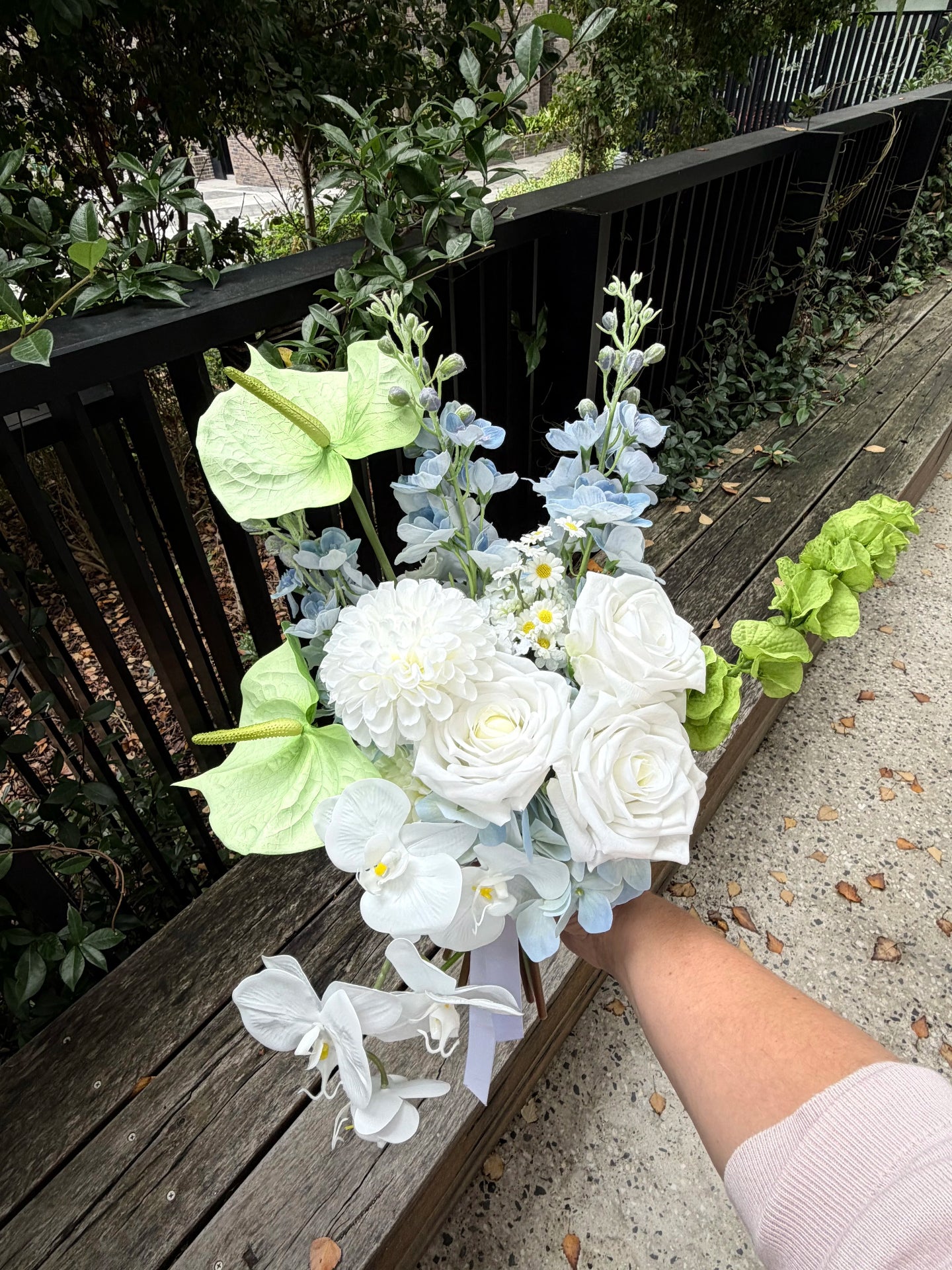 Bouquet of flowers held by a person on a wooden deck with greenery in the background