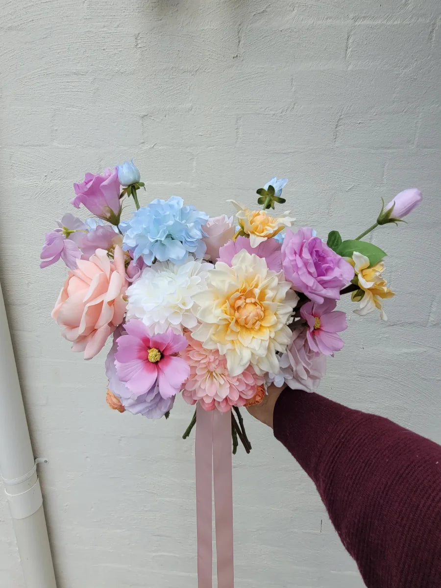 Faux wedding bouquet of colourful flowers held by a person against a plain background