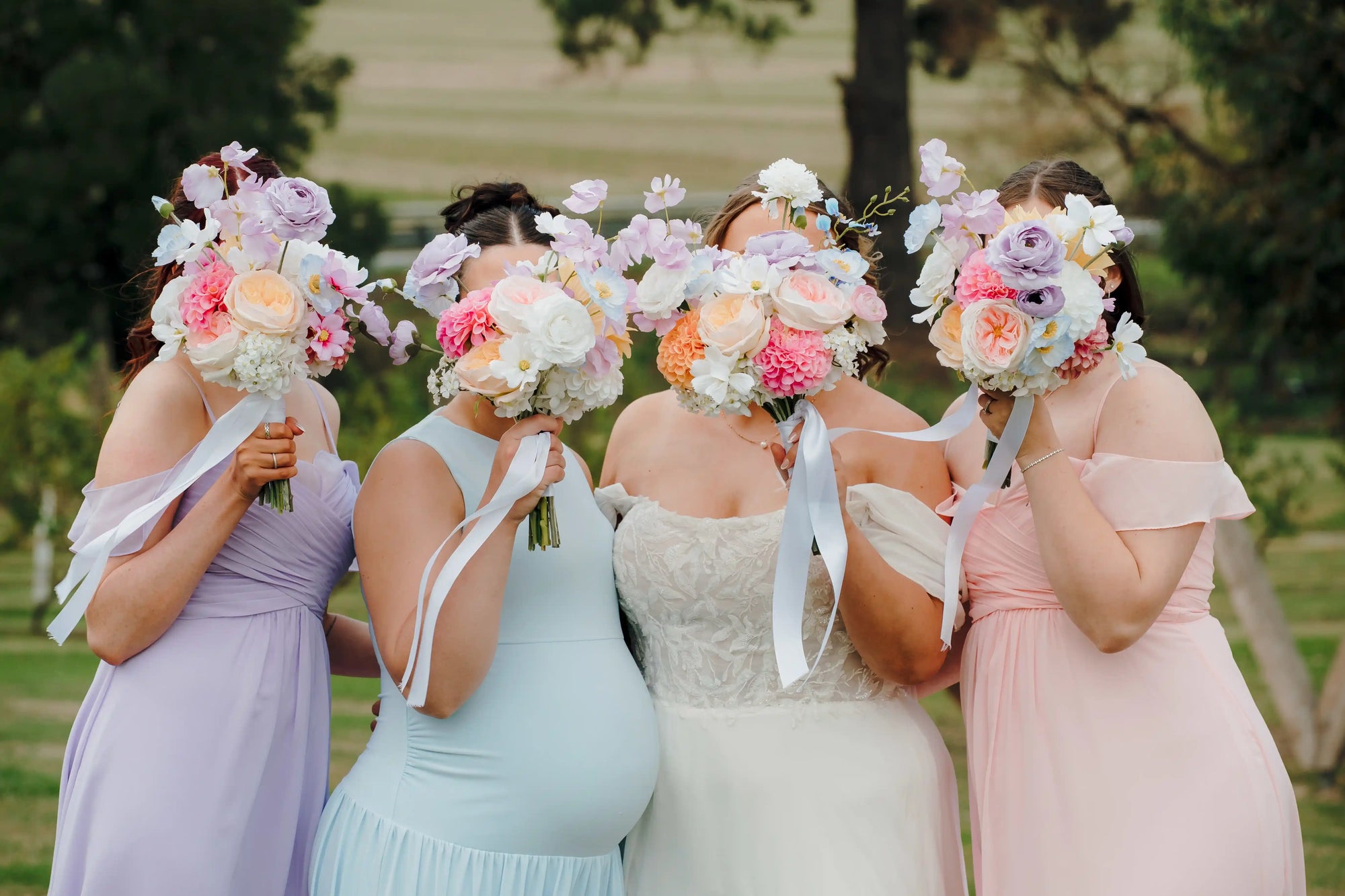 Bride and bridesmaids posing with pastel wedding bouquets in front of their face