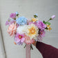 Bouquet of colorful flowers held by a hand against a light gray background