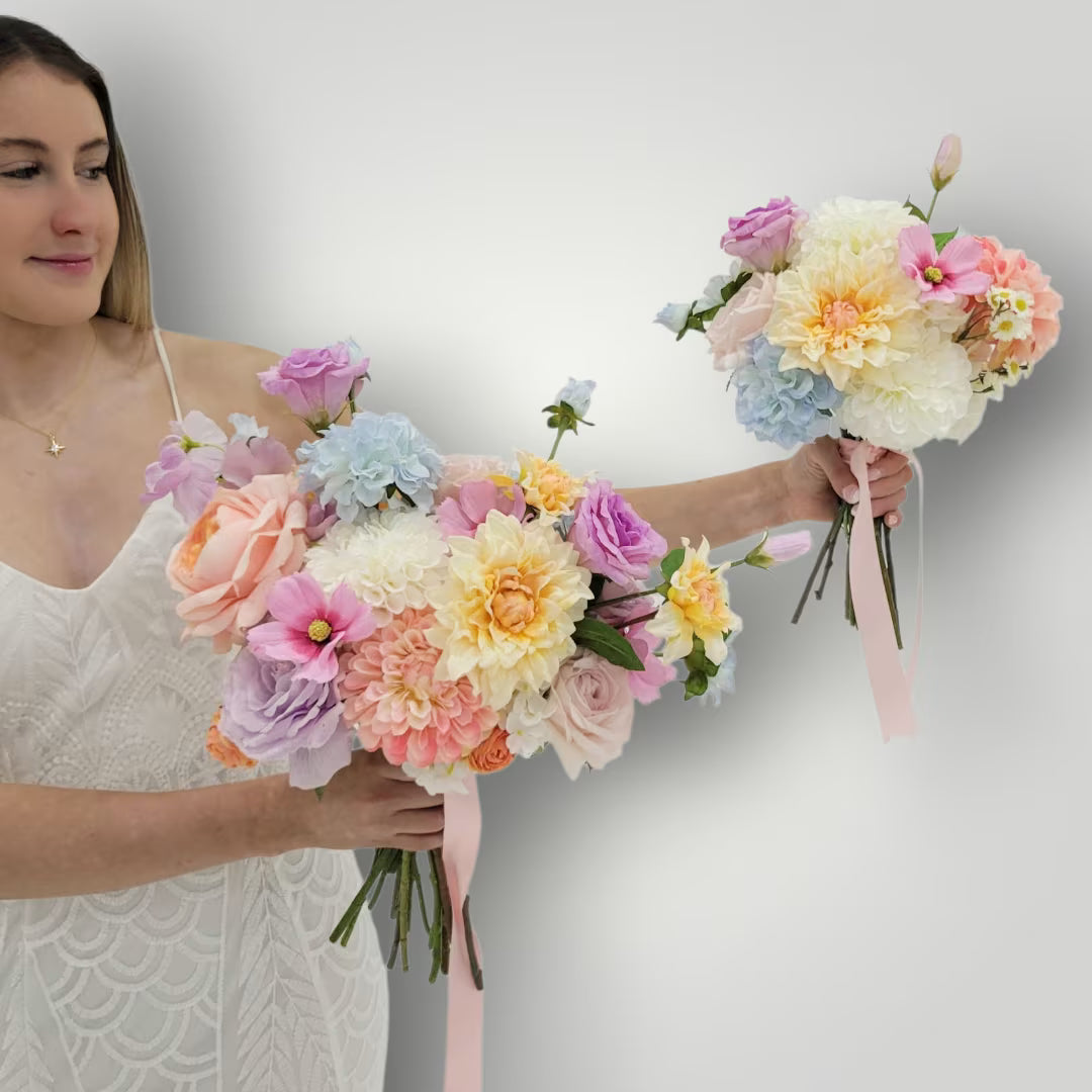 Woman holding two bouquets of pastel flowers against a plain background