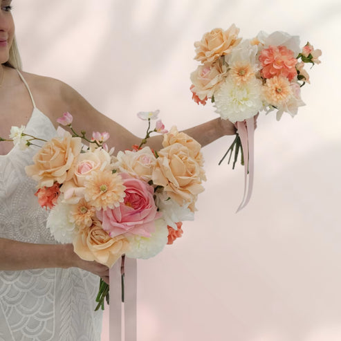 Two hands holding two peach and white wedding bouquets