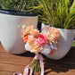 Bridal bouquet of flowers with a pink ribbon on a wooden surface with plants in the background
