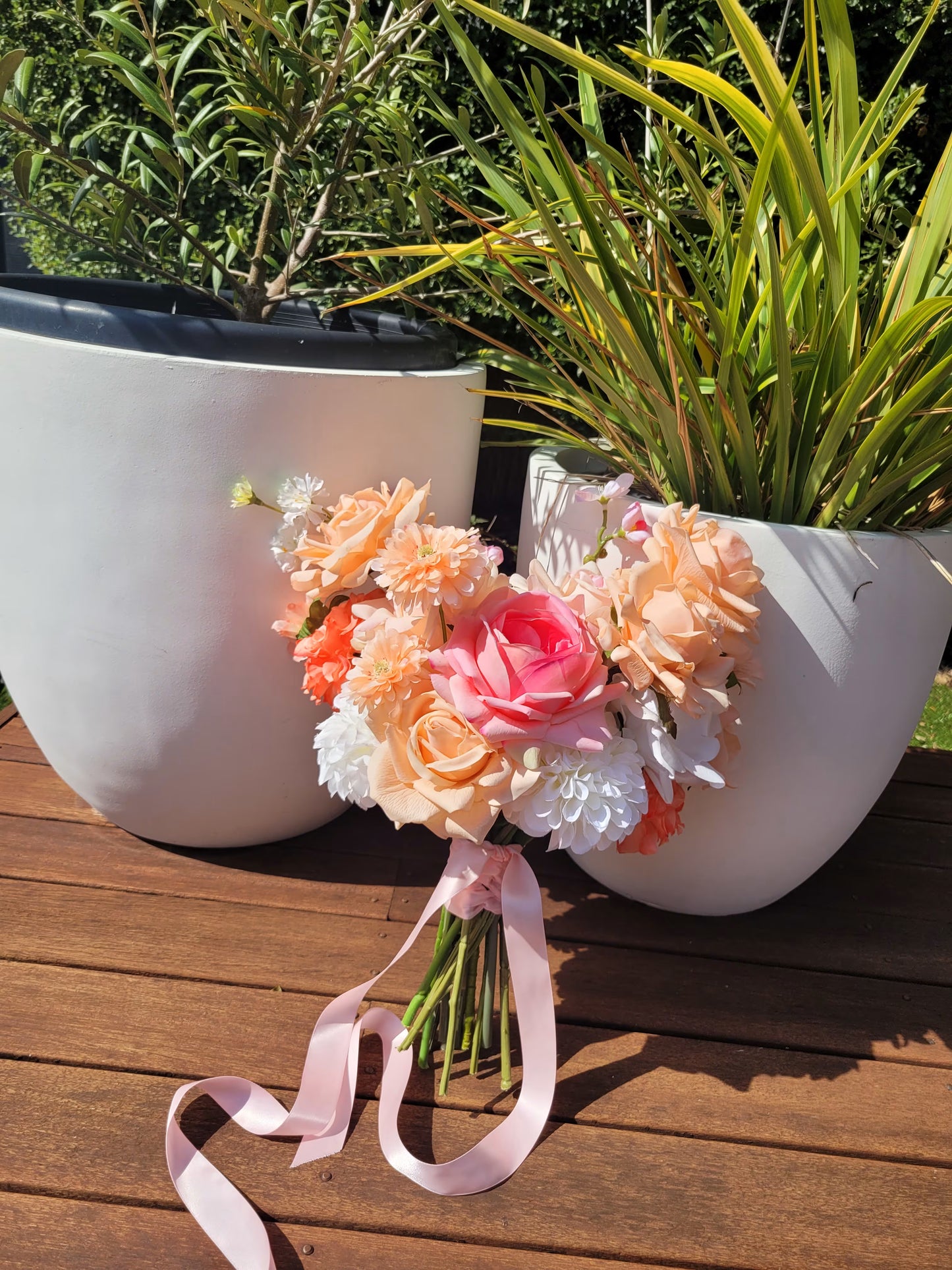 Bridal bouquet of flowers with a pink ribbon on a wooden surface with plants in the background