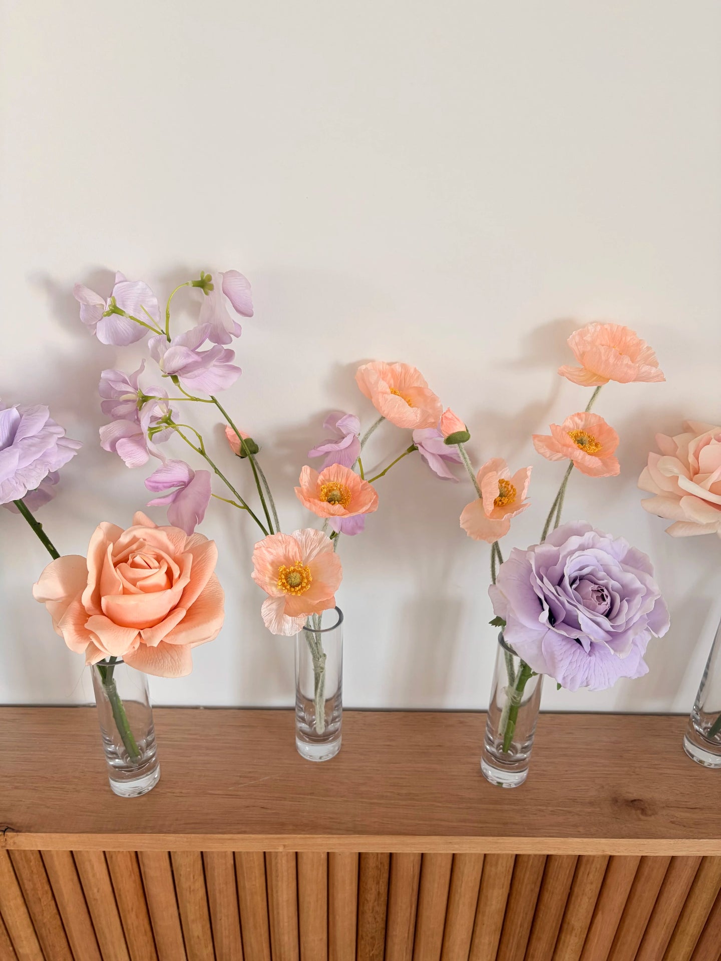 Decorative artificial wedding flowers in bud vases on a wooden surface with a white wall background