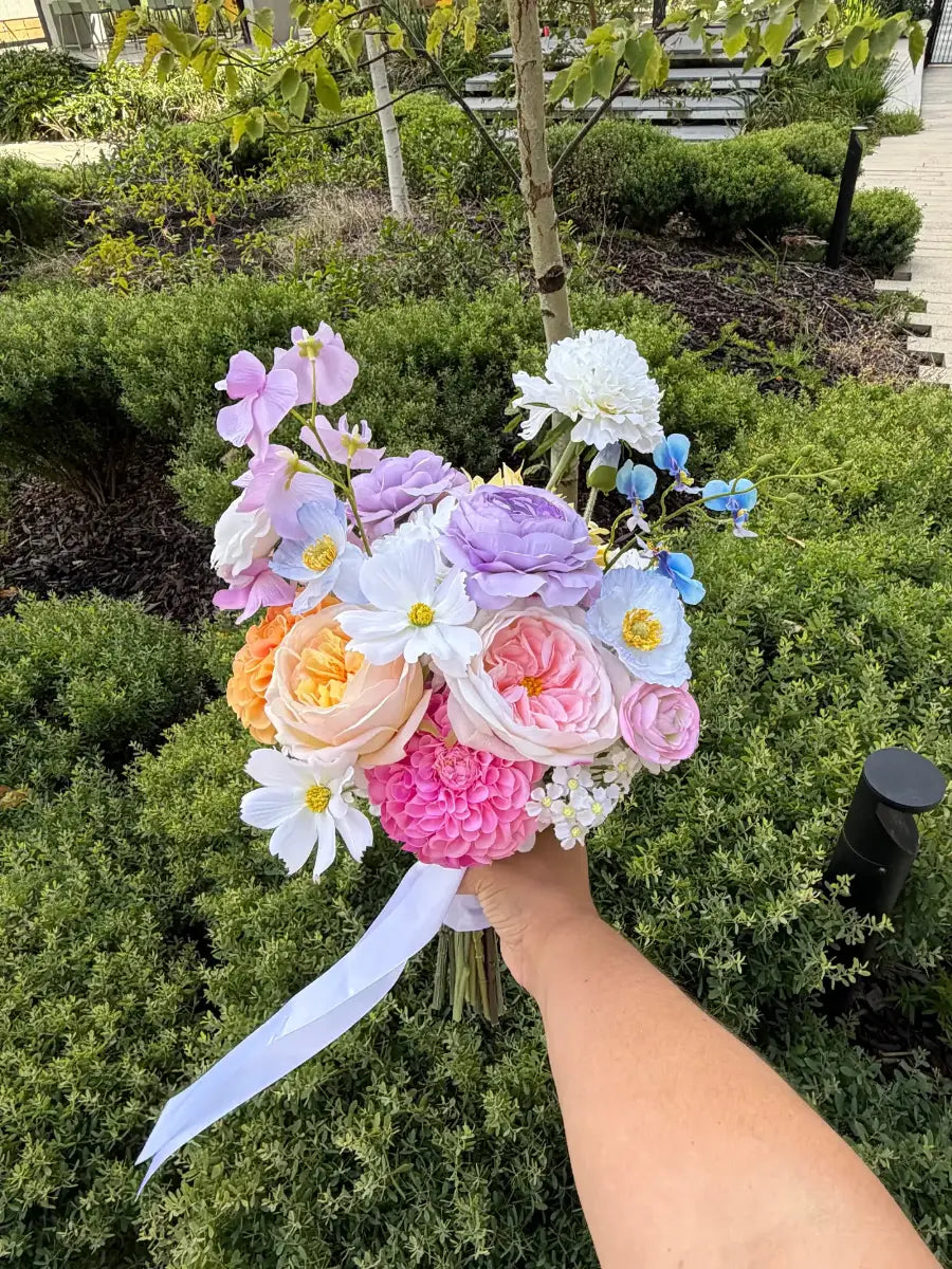 Bouquet of colourful flowers held in front of green bushes