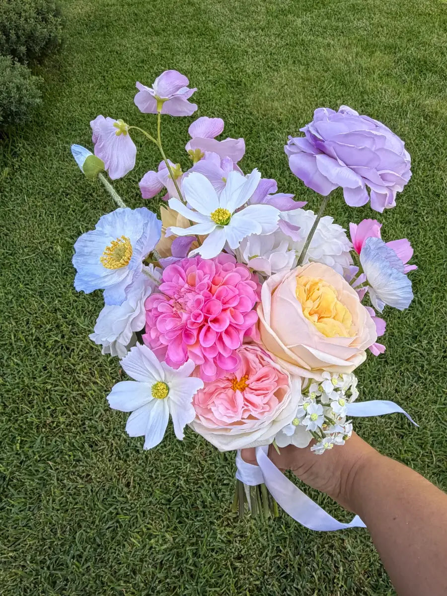 Bouquet of colourful flowers held by a hand on grass