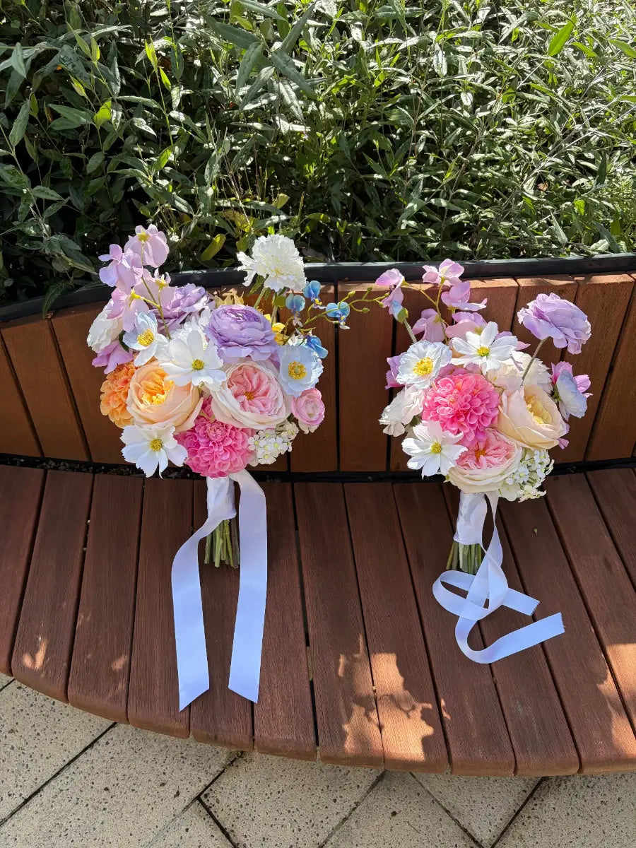 Two artificial wedding bouquets on a wooden surface with greenery in the background