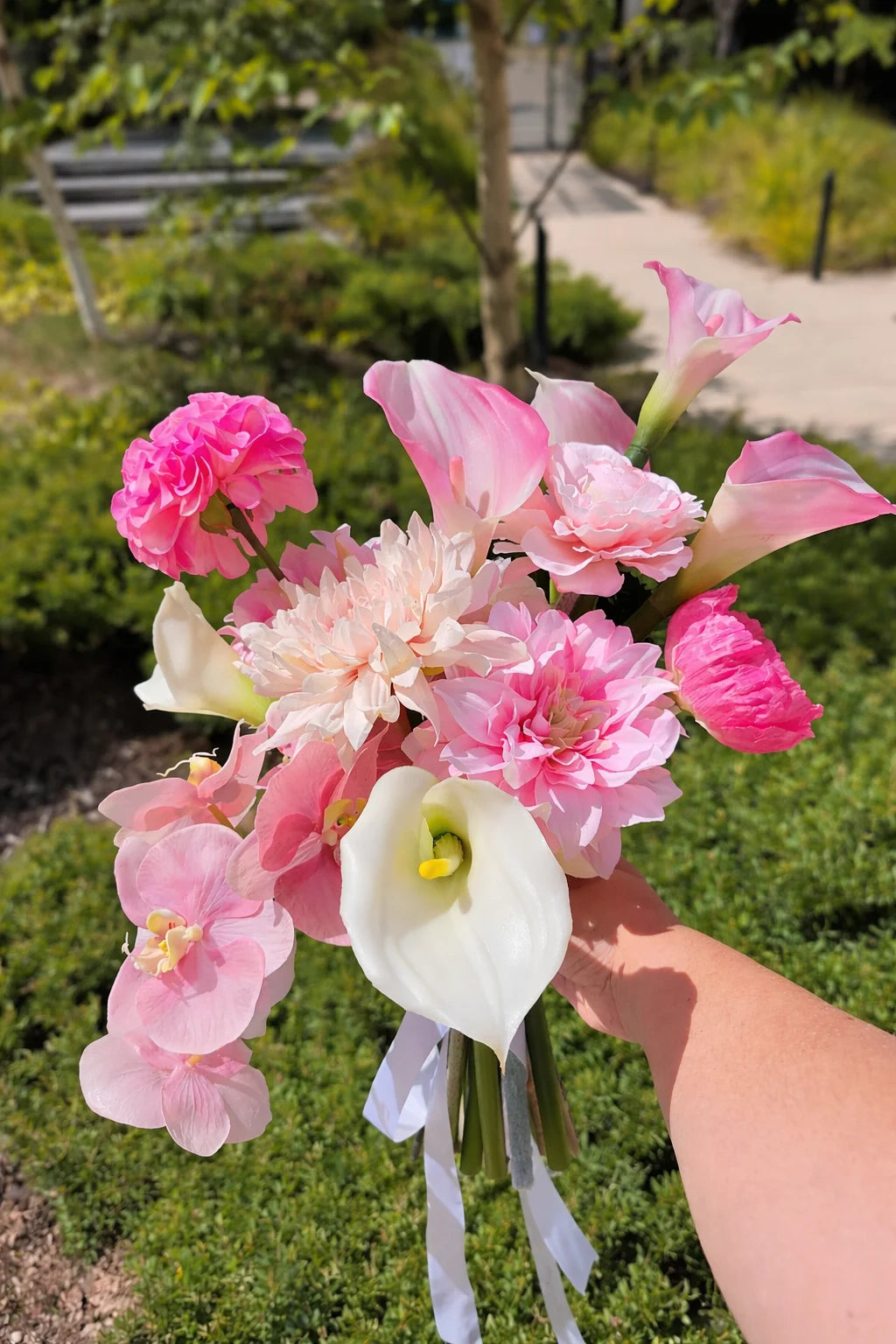 Bouquet of pink and white flowers held by a person with greenery in the background
