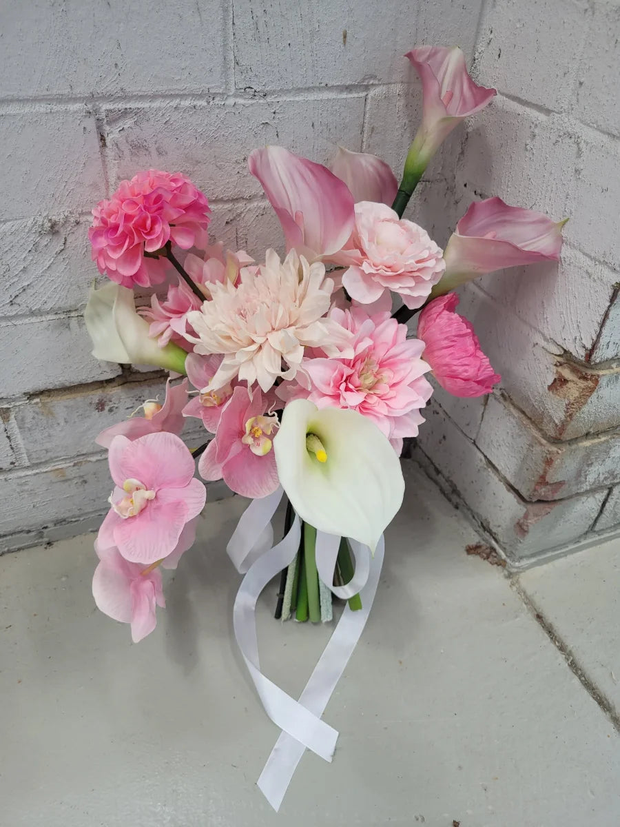 Bouquet of pink and white flowers with a white ribbon against a textured wall.