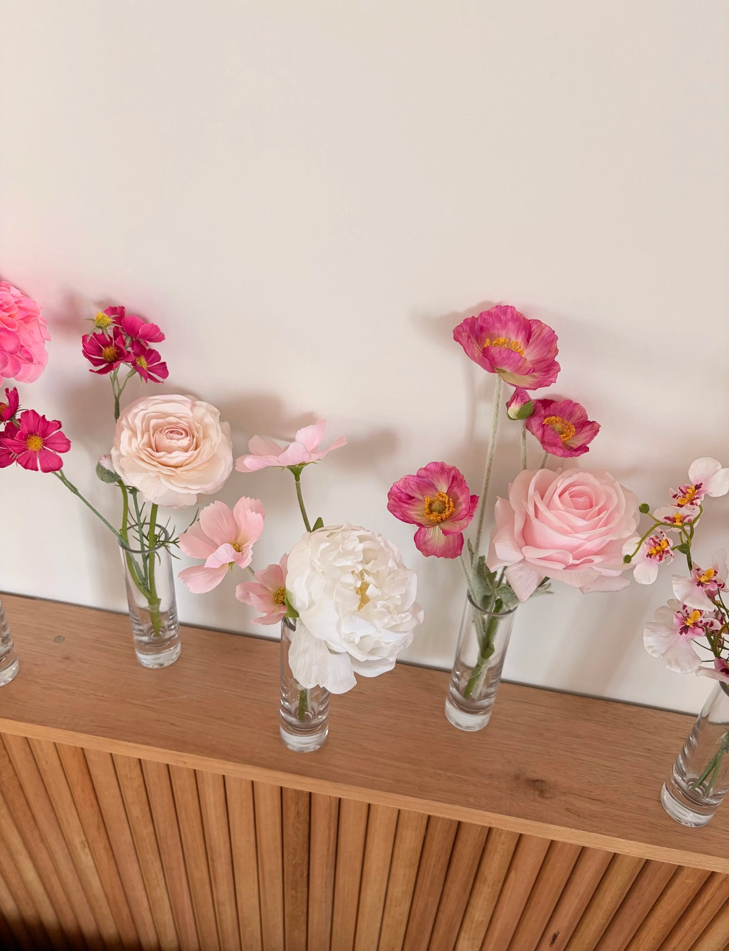 Bud vases with small flower arrangements on a wooden surface against a white wall