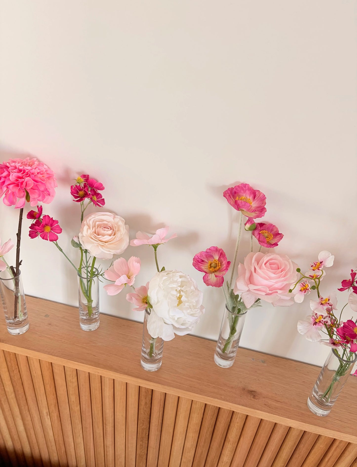 Bud vases with pink and white flowers on a wooden surface