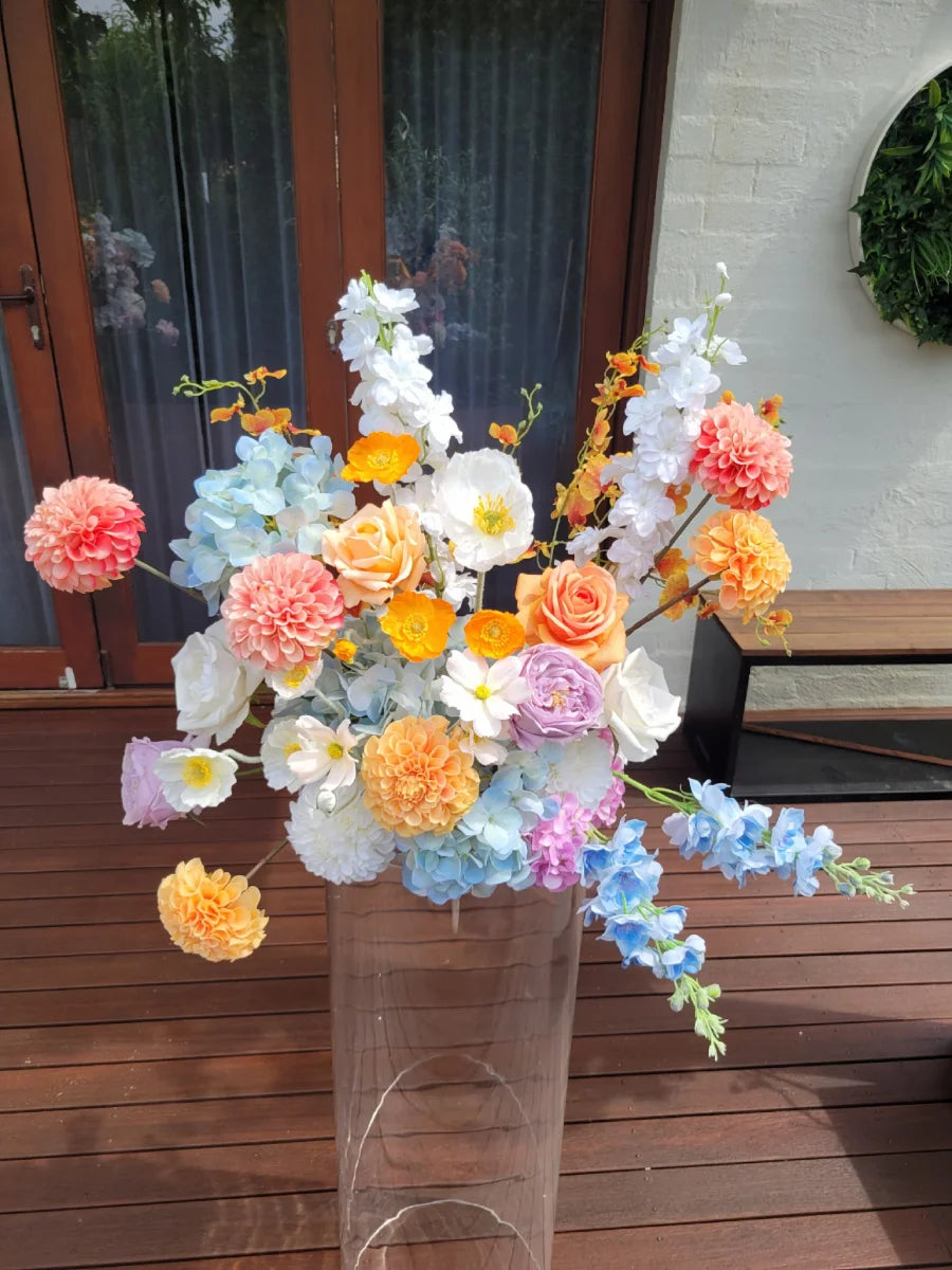 Colourful  artificial flower arrangement in a clear plinth on a wooden surface
