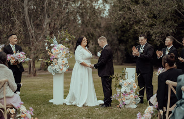 Wedding ceremony with a couple holding hands in front of floral arrangements and guests clapping.