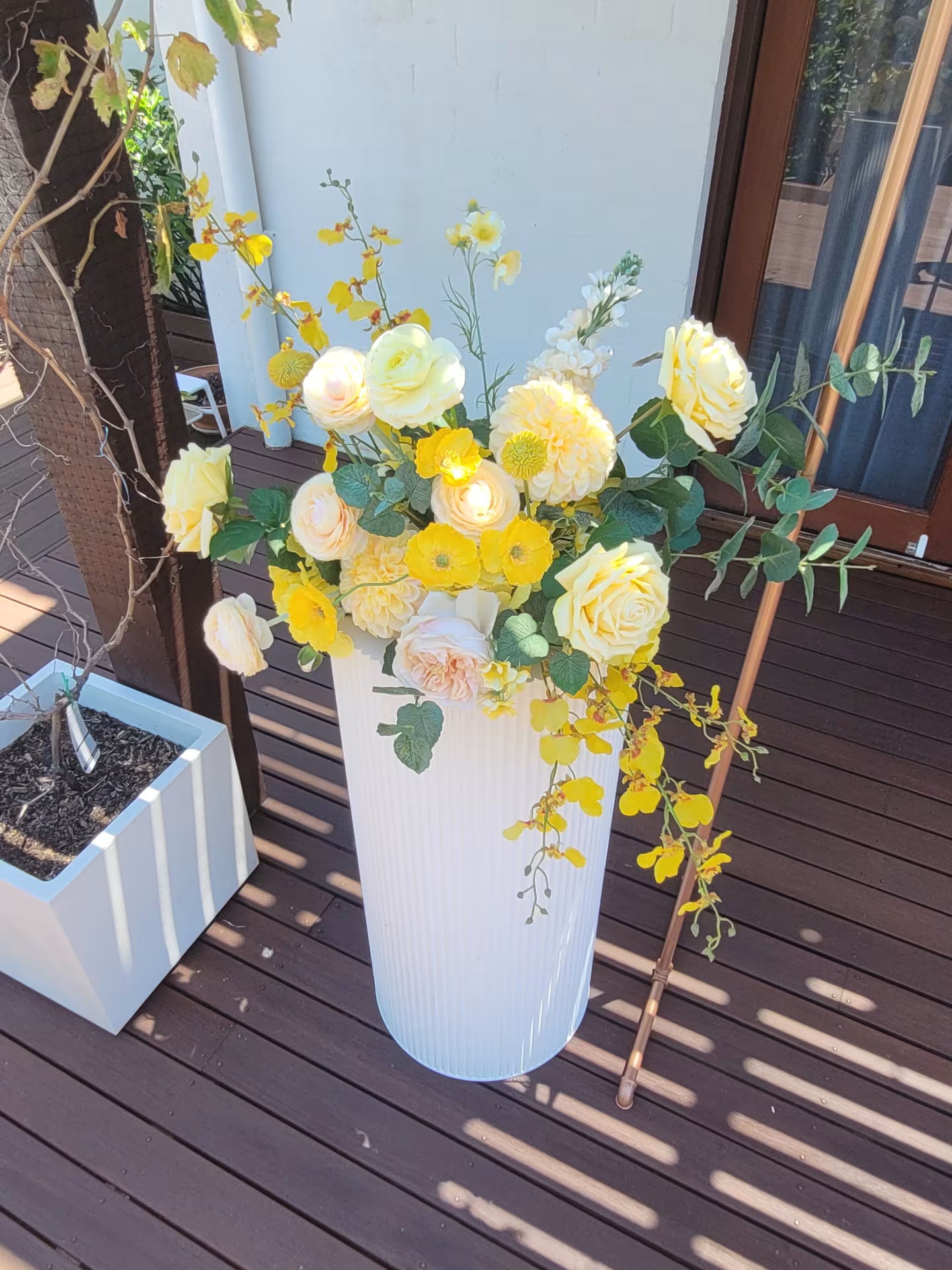 White plinth with a large yellow flower arrangement on a wooden deck