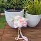 Bridal bouquet of pink and white flowers with ribbons on a wooden table with potted plants in the background.