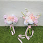 Two flower bouquets with pink ribbons on a grassy surface.
