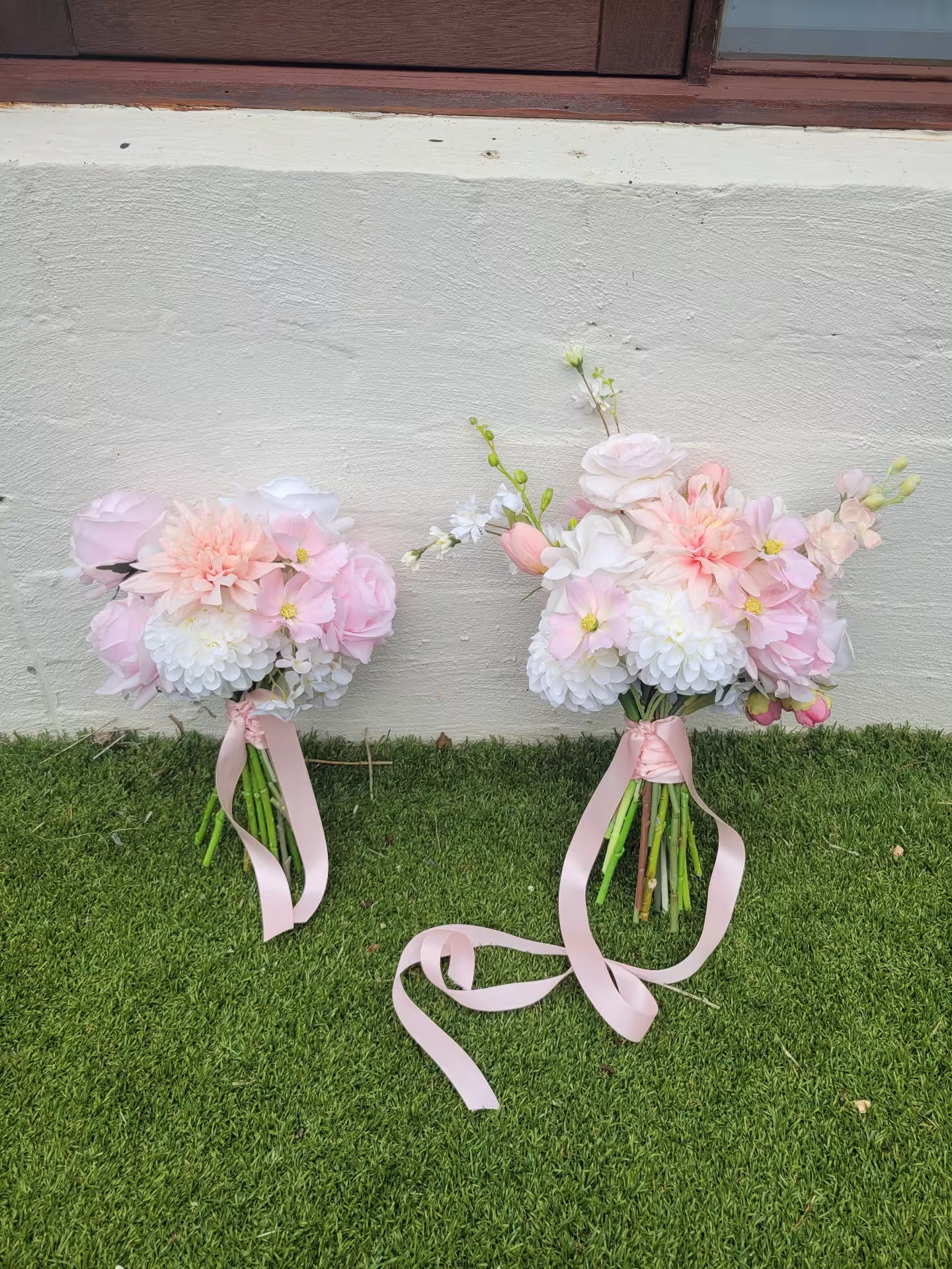Two flower bouquets with pink ribbons on a grassy surface.