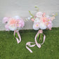 Two floral bouquets with pink ribbons on a grassy surface.