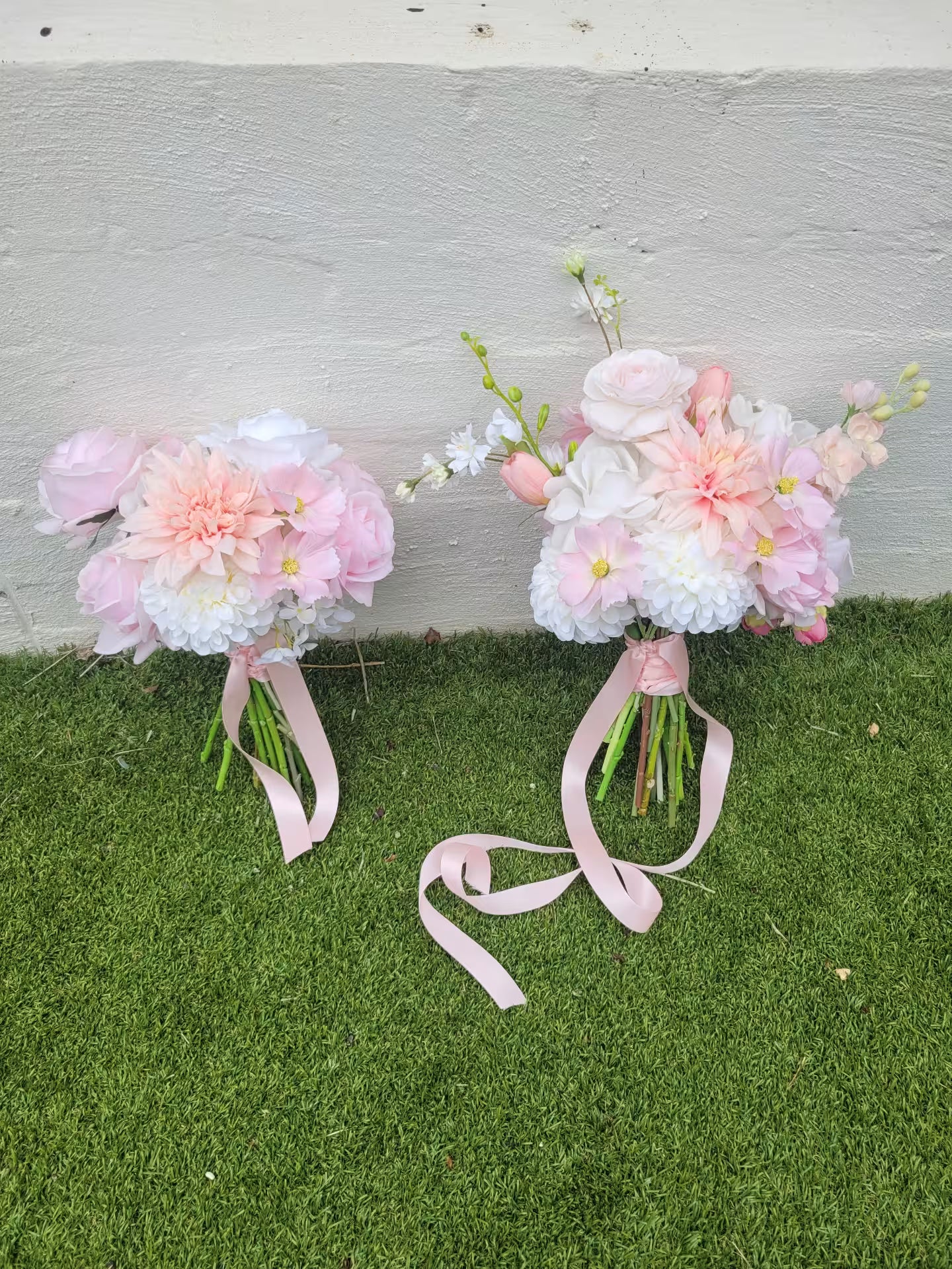Two floral bouquets with pink ribbons on a grassy surface.