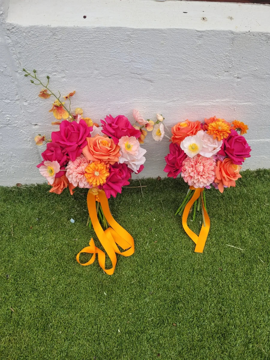Two artificial wedding bouquets with colourful flowers and ribbons on a grassy surface.