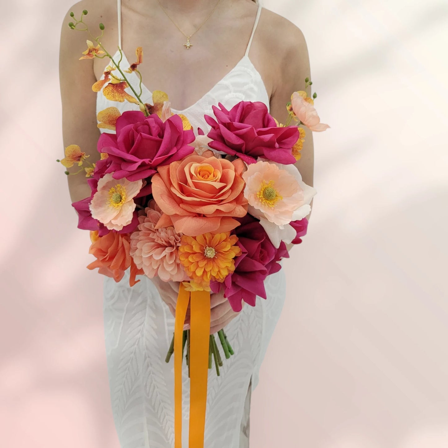 Faux wedding bouquet of colourful flowers held by a person wearing a white dress against a soft pink background