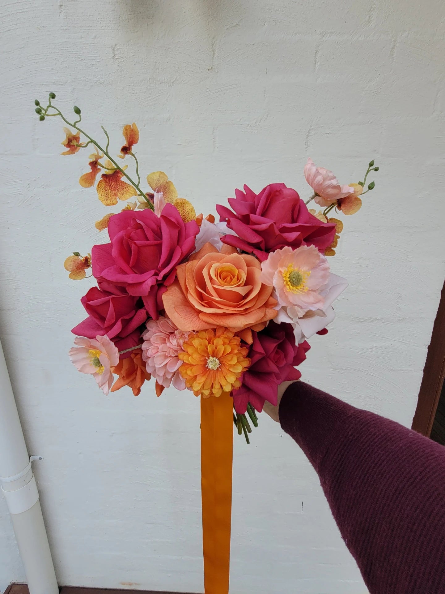 Wedding bouquet of colourful flowers held by a person against a white wall