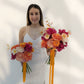 Woman in a white dress holding two bouquets of flowers with orange ribbons against a plain background