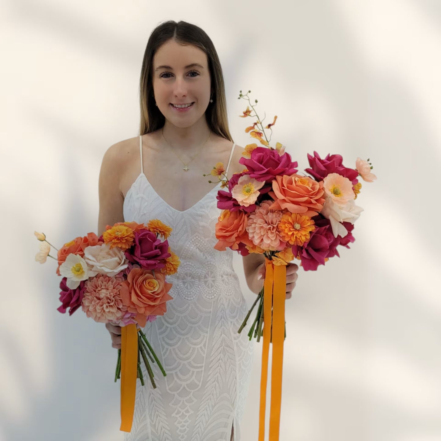 Woman in a white dress holding two bouquets of flowers with orange ribbons against a plain background