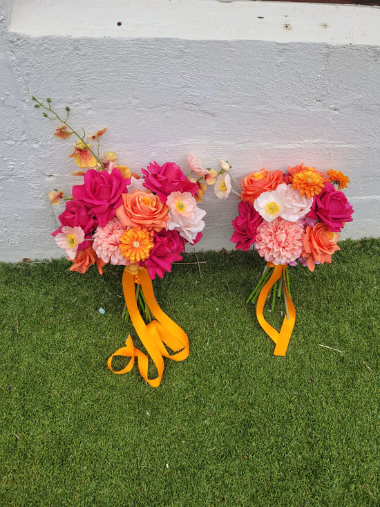 Two floral bouquets with colorful flowers and yellow ribbons on a grassy surface.