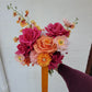 Colorful bridal bouquet held by a person against a white wall