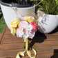 Bouquet of flowers with yellow, pink, and white colors on a wooden surface with plant pots in the background.