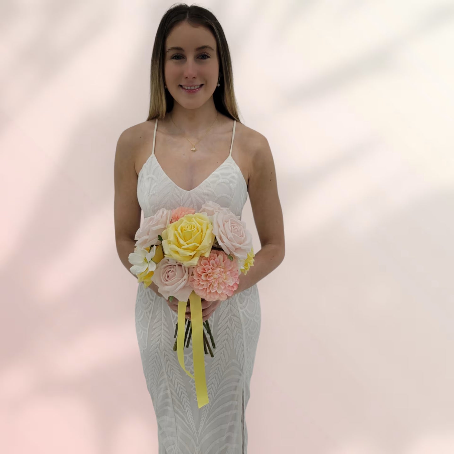 Woman in a white lace dress holding a bouquet of flowers against a soft pink background