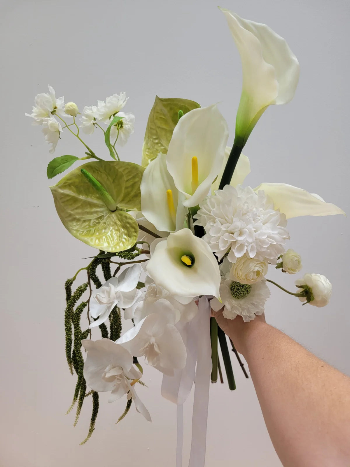 Bouquet of white and green flowers held by a hand against a gray background