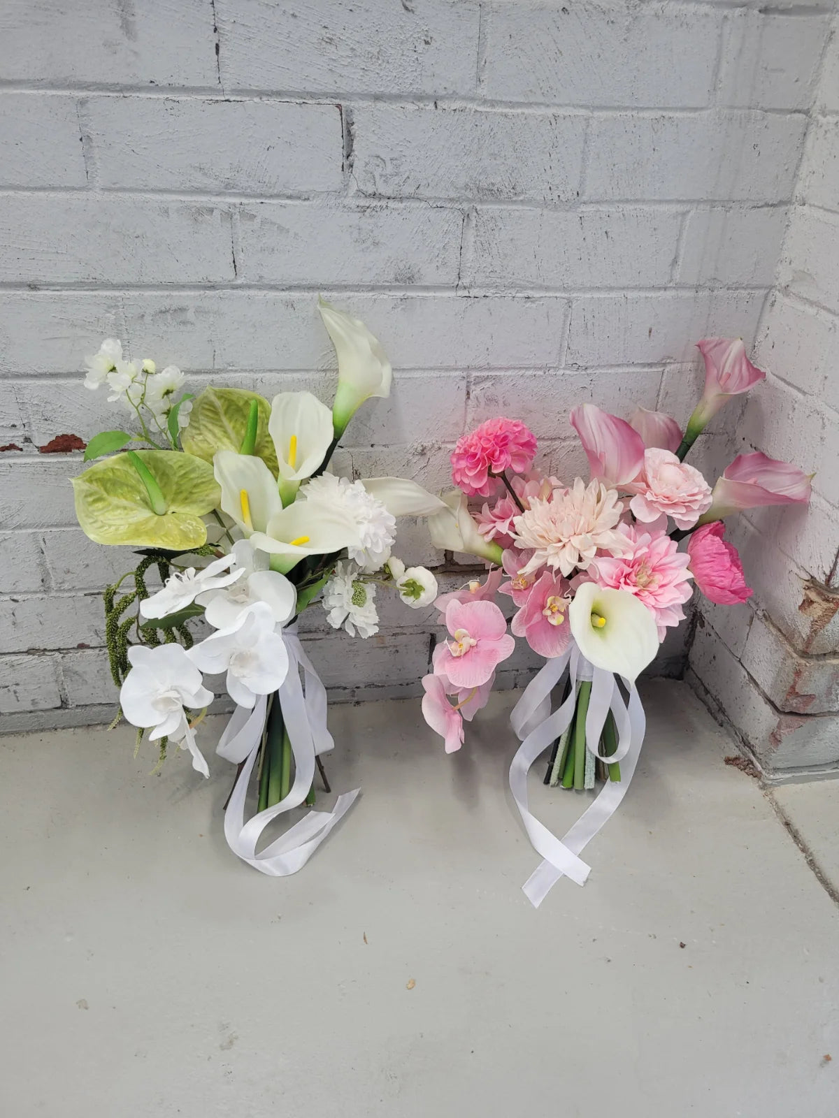 Two floral bouquets with ribbons against a white brick wall.