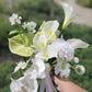 Hand holding a white calla lily bouquet against a blurred background in a garden setting