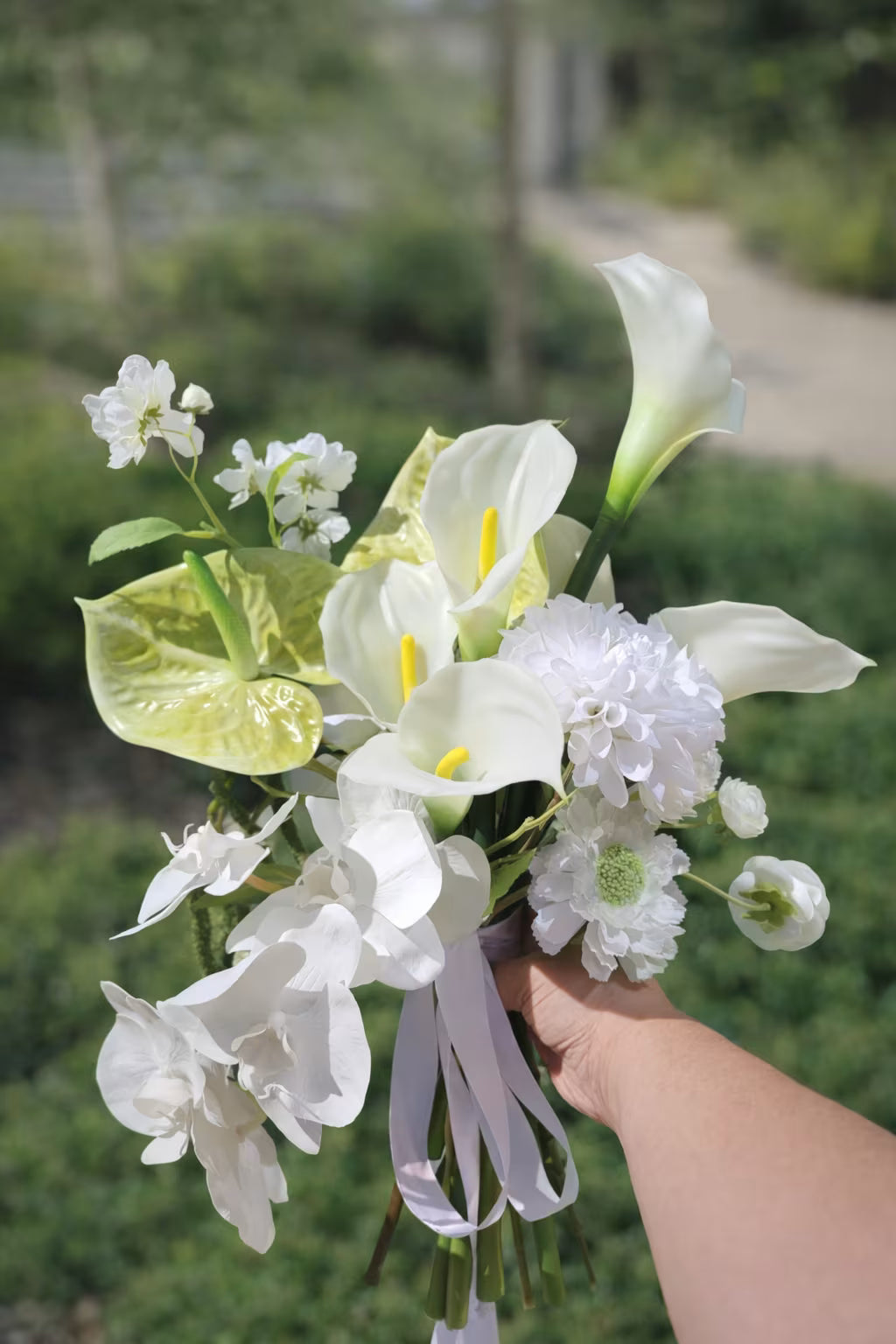 Hand holding a white calla lily bouquet against a blurred background in a garden setting