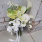 Bouquet of white and green flowers with ribbons against a brick wall.