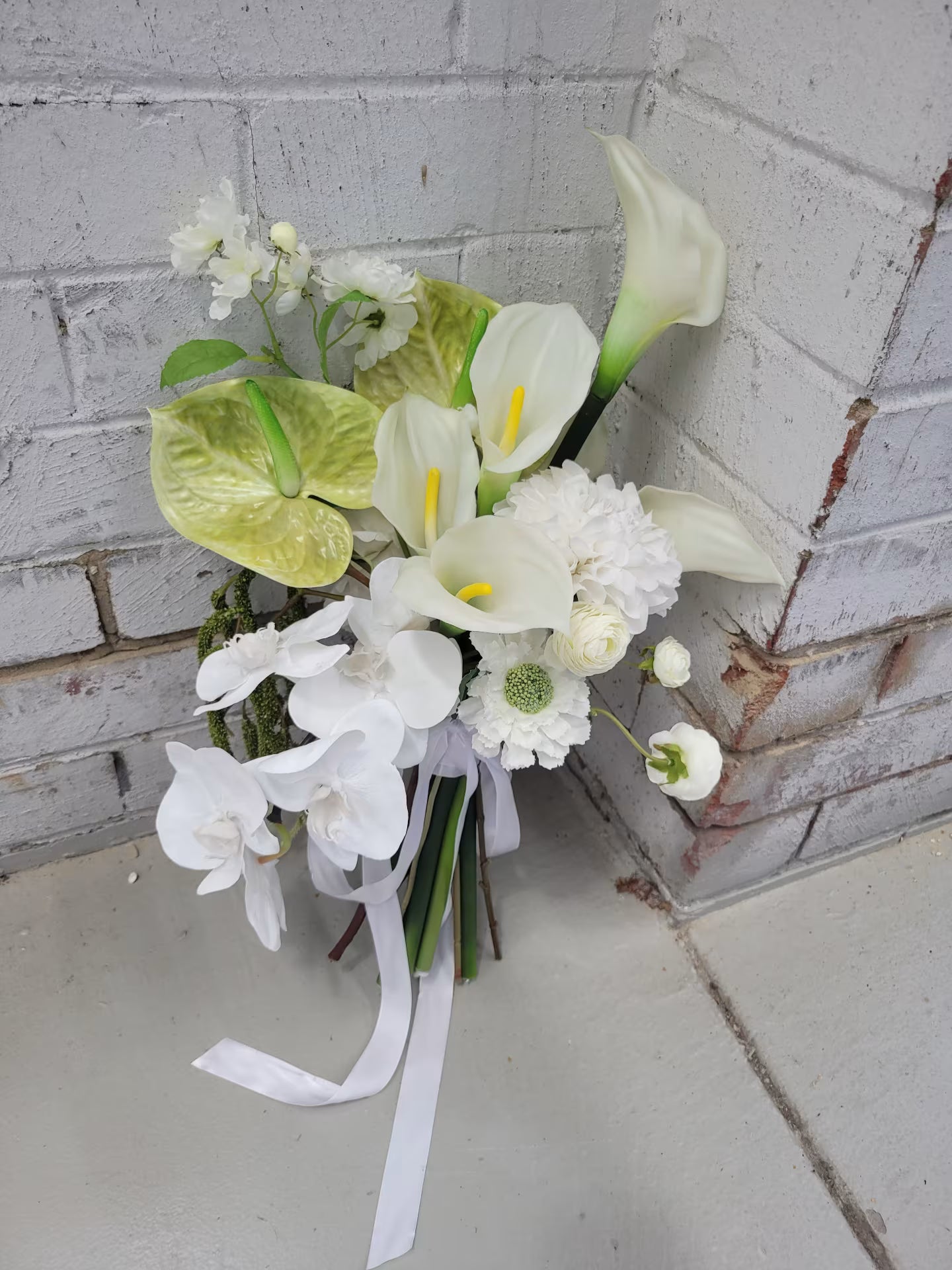 Bouquet of white and green flowers with ribbons against a brick wall.