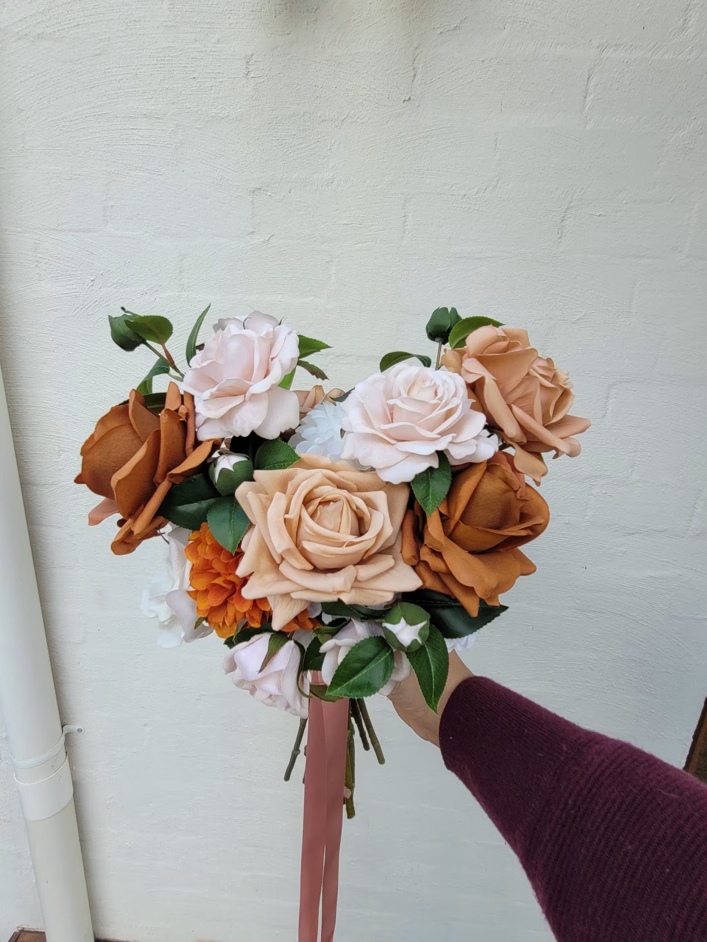 Bridal bouquet of flowers held by a person against a white wall