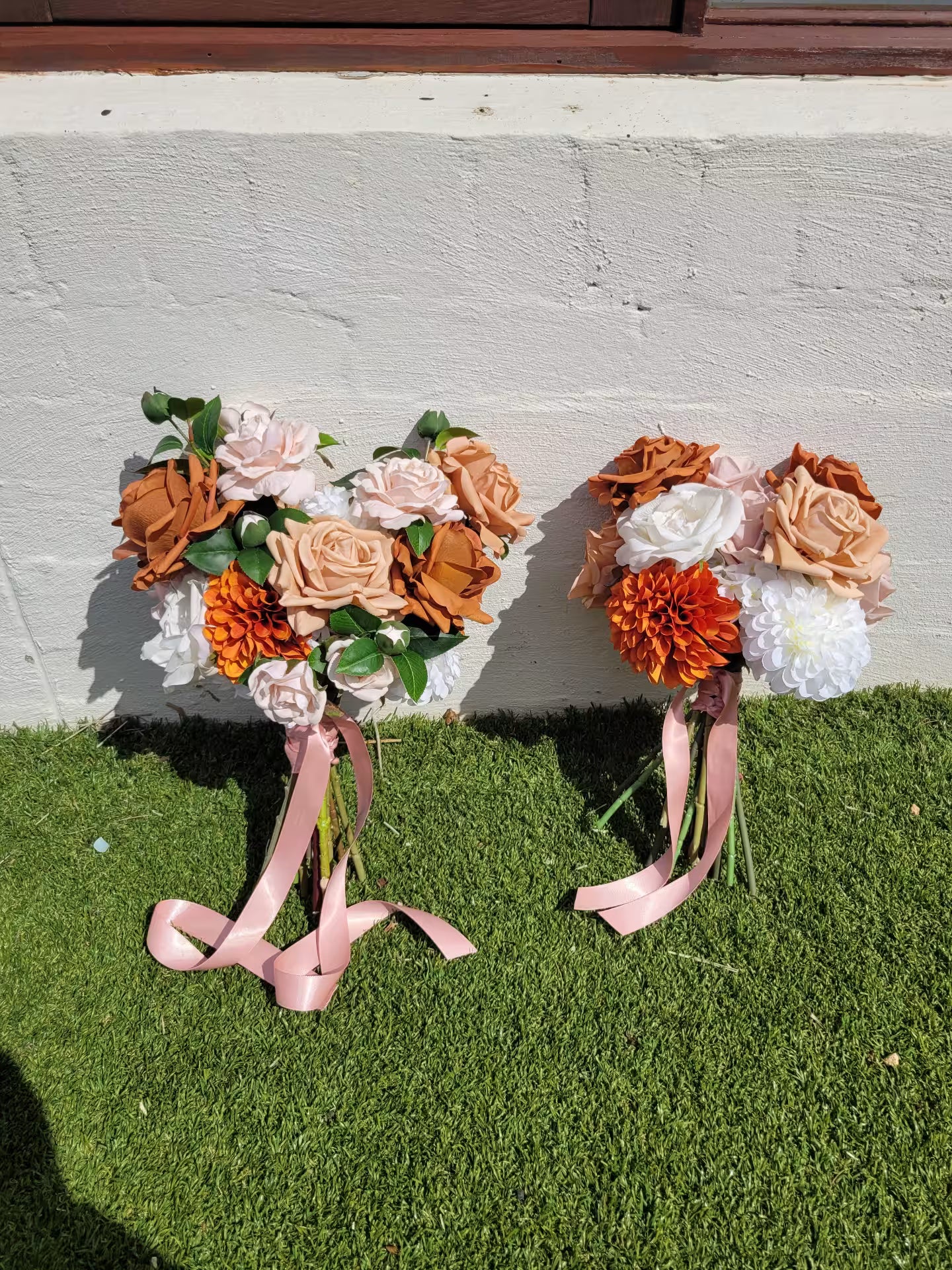 Two wedding bouquets on a grassy surface with a concrete wall background.